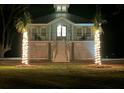 Night view of a charming elevated coastal home with lighted palm trees and an inviting warm glow from within at 16 Oakwood Ln, Edisto Island, SC 29438