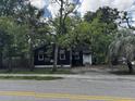 Modest single-story home featuring a black exterior, brick foundation, awning accents and mature trees at 2334 Kent Ave, North Charleston, SC 29405