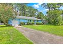 A cute, light blue house with attached garage surrounded by grass, trees, and a long concrete driveway at 312 Woodward Blvd, Summerville, SC 29483