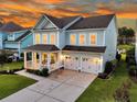 Elegant two-story home boasts a cozy front porch, double garage, and lush landscaping with a picturesque sunset backdrop at 292 Calm Water Way, Summerville, SC 29486