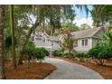 View of the gray home down long driveway, featuring lush landscaping with trees, and a two-car garage at 2645 Gnarled Pine, Seabrook Island, SC 29455