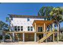 A new beach house exhibits a spacious elevated deck and stairs, with lush vegetation and a clear blue sky backdrop at 817 Cheehaw St, Edisto Island, SC 29438