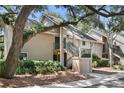 Inviting exterior of a tan condo building with stairs to the second-floor entry under mature tree canopy at 146 High Hammock Villas, Seabrook Island, SC 29455