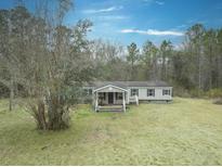 Tan mobile home with covered porch and large yard, surrounded by trees at 139 Yellowstone Ln, Ridgeville, SC 29472