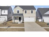 Two-story tan house with a white garage door and landscaping at 141 Wood Sage Run, Summerville, SC 29485