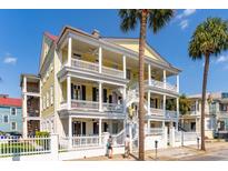 3 story yellow home with wrap around porches, white railings, and palm trees at 212 Calhoun, Charleston, SC 29401