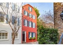 A narrow red brick home with blue shutters is flanked by white brick house and mature trees at 32 Tradd St, Charleston, SC 29401