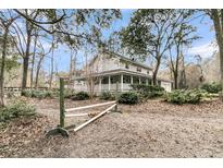 Charming two-story home with a large wrap-around porch, surrounded by mature trees and lush landscaping at 135 Rapture Ln, Wando, SC 29492