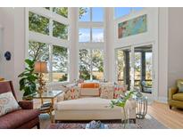 Bright living room features soaring windows and a cozy chaise lounge with views of the serene marsh at 2250 Bohicket Creek Pl, Seabrook Island, SC 29455