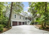Stunning exterior showcasing the home's architectural design, three-car garage, and lush, mature landscaping at 2932 Old Drake Dr, Seabrook Island, SC 29455