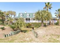 Charming coastal home featuring a green metal roof, white siding, and a welcoming front porch surrounded by palm trees at 214 Charleston Blvd, Isle of Palms, SC 29451