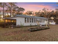 Charming white home featuring a screened-in porch and multiple windows, surrounded by mature trees and inviting landscaping at 4680 Bears Bluff Rd, Wadmalaw Island, SC 29487