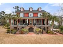 Inviting two-story red home featuring a brick foundation, covered porch, and lush tropical landscaping at 2786 Parkers Landing Rd, Mount Pleasant, SC 29466