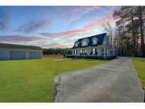 Charming home with a long driveway, a lush green lawn, and a detached garage under a colorful sunset sky at 516 & 508 Robnshers Pl, Ridgeville, SC 29472