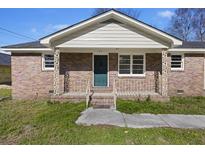 Charming brick home featuring a quaint front porch, complemented by manicured landscaping and a welcoming green door at 127 Ridge Rd, Summerville, SC 29485