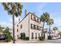 Stately stucco home boasts traditional design, brown shutters, and meticulously landscaped yard with mature palm trees at 40 State St # 1, Charleston, SC 29401