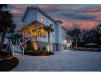 Stunning three-story home with a brick driveway and beautiful tropical landscaping at dusk at 1648 Home Farm Rd, Mount Pleasant, SC 29464