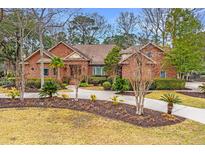 Charming brick home featuring a well-manicured lawn with mature trees, landscaping, and a curved walkway at 4140 Club Course Dr, North Charleston, SC 29420