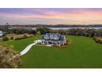 Stunning aerial view of a modern farmhouse estate with sprawling lawn, mature trees, and waterfront access at sunset at 2621 Anchor Watch Dr, Wadmalaw Island, SC 29487