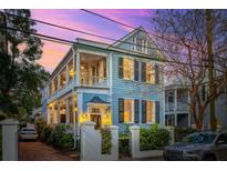 Charming two-story home with double porches, shutters, and lush landscaping at twilight at 100 Queen St, Charleston, SC 29401