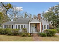 Charming single-story home with gray siding, brick chimney, manicured landscaping, and inviting front porch at 105 S Palmetto St, Summerville, SC 29483