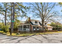 Charming two-story home featuring a screened porch, picket fence, brick accents, and mature trees at 74 6Th Ave, Charleston, SC 29403