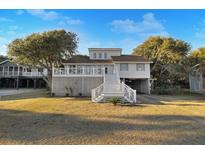 Charming coastal home with a white exterior, elevated design, and beautiful landscaping on a sunny day at 707 Palmetto Blvd, Edisto Island, SC 29438