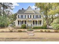 Charming two-story home featuring a welcoming front porch, black shutters, mature trees and manicured lawn at 710 S Main St, Summerville, SC 29483