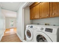 Convenient laundry room featuring a modern, front-loading washer and dryer, with ample storage in wooden cabinets at 15 Loch Carrun Ter, Charleston, SC 29414