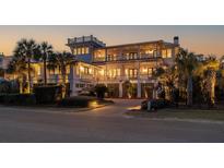 Stunning multi-story home with inviting balconies, lush landscaping, and a brick driveway at twilight at 3030 Marshall Blvd, Sullivans Island, SC 29482