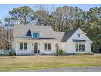 Charming white farmhouse with a covered front porch, black window trim, and an American flag at 1174 Hitchfield Ln, Awendaw, SC 29429