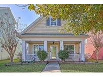 Charming yellow two-story home featuring a cozy front porch with white columns and manicured landscaping at 303 Crossandra Ave, Summerville, SC 29483