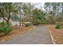 Gravel driveway leads to a two-car garage surrounded by mature trees and natural landscaping at 9030 Ethel Rd, North Charleston, SC 29406