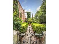 View of the garden through a black wrought iron gate and leading to a brick building with greenery at 309 Meeting St # 19, Charleston, SC 29401