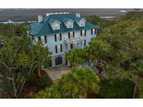Stately two-story home with a green metal roof and grand entrance surrounded by mature trees and lush landscaping at 944 Hammocks Way, Edisto Island, SC 29438