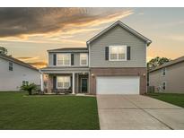 Charming two-story home with a manicured lawn, brick accents, and a two-car garage beneath a golden sky at 233 Old Carolina Dr, Goose Creek, SC 29445