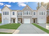 Charming townhomes featuring attached garages, concrete driveway, and manicured lawns against a blue, partly cloudy sky at 8745 Silver Perch Ln, North Charleston, SC 29420