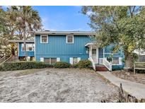 Charming blue two-story home with a well-manicured lawn and a welcoming front porch and mature landscaping at 702 E Erie Ave, Folly Beach, SC 29439