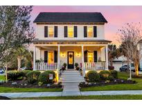 Charming two-story white home with a welcoming front porch, well-manicured landscaping, and warm exterior lighting at twilight at 1525 Harriman St, Mount Pleasant, SC 29466