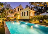 Inviting pool area with elegant lighting, patio furniture, and a view of the charming yellow house at twilight at 171 Broad St, Charleston, SC 29401