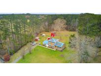 Expansive aerial view of a stone house with a blue metal roof and red barns, surrounded by a lush green lawn and tall trees at 276 S Railroad Ave, Harleyville, SC 29448