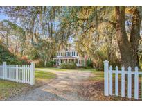 Charming two-story home with white picket fence, lush landscaping, and grand trees draped in Spanish moss at 8115 Adams Run School Rd, Adams Run, SC 29426