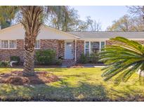 Charming brick home with a well-manicured lawn and mature palm trees in a sunny front yard at 689 Port Cir, Charleston, SC 29412