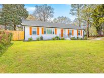 Charming one-story home with a manicured lawn and bright orange shutters and door at 7665 Picardy Pl, North Charleston, SC 29420