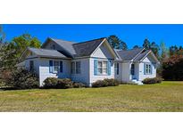 Charming white home featuring a gray roof and vibrant blue shutters, surrounded by lush landscaping at 8524 Cane Branch Rd, Ruffin, SC 29475