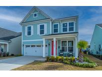 Charming two-story home with pale blue siding, white trim, bright red door, and well-manicured landscaping at 1081 Magnolia Warbler Way, Ravenel, SC 29470