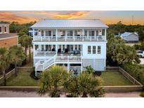 Beautiful multi-story home with a metal roof, white trim, and multiple decks overlooking manicured lawn with palm trees at 1702 Palmetto Blvd, Edisto Island, SC 29438