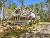Charming home featuring a wraparound porch, lush landscaping, and an American flag, perfect for relaxation at 1212 Pinopolis Rd, Moncks Corner, SC 29461