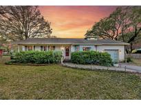 Charming one-story home with lush landscaping, brick walkway and inviting covered porch at sunset at 633 Schooner Rd, Charleston, SC 29412