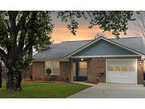 Charming brick home with an attached garage, complemented by a lush green lawn and mature trees at 8530 Bentwood Dr, North Charleston, SC 29406